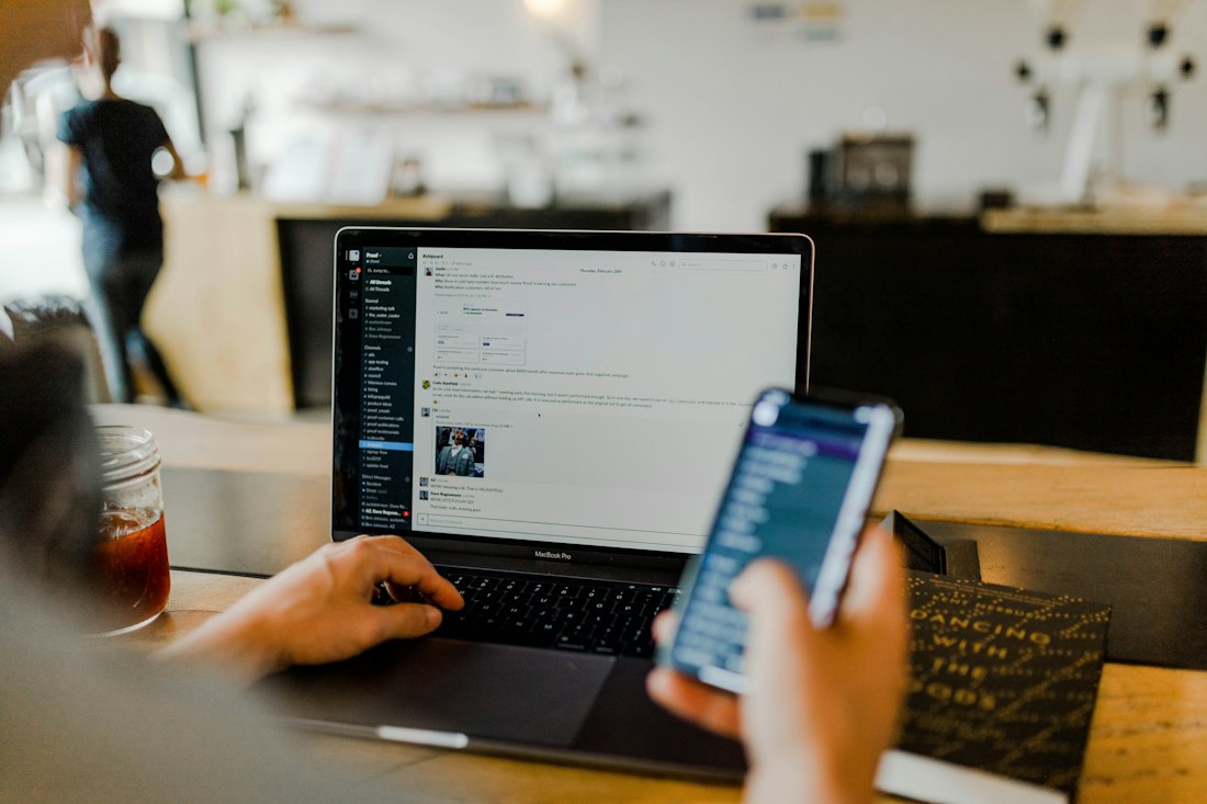 A customer checking their banking app on a phone next to a laptop