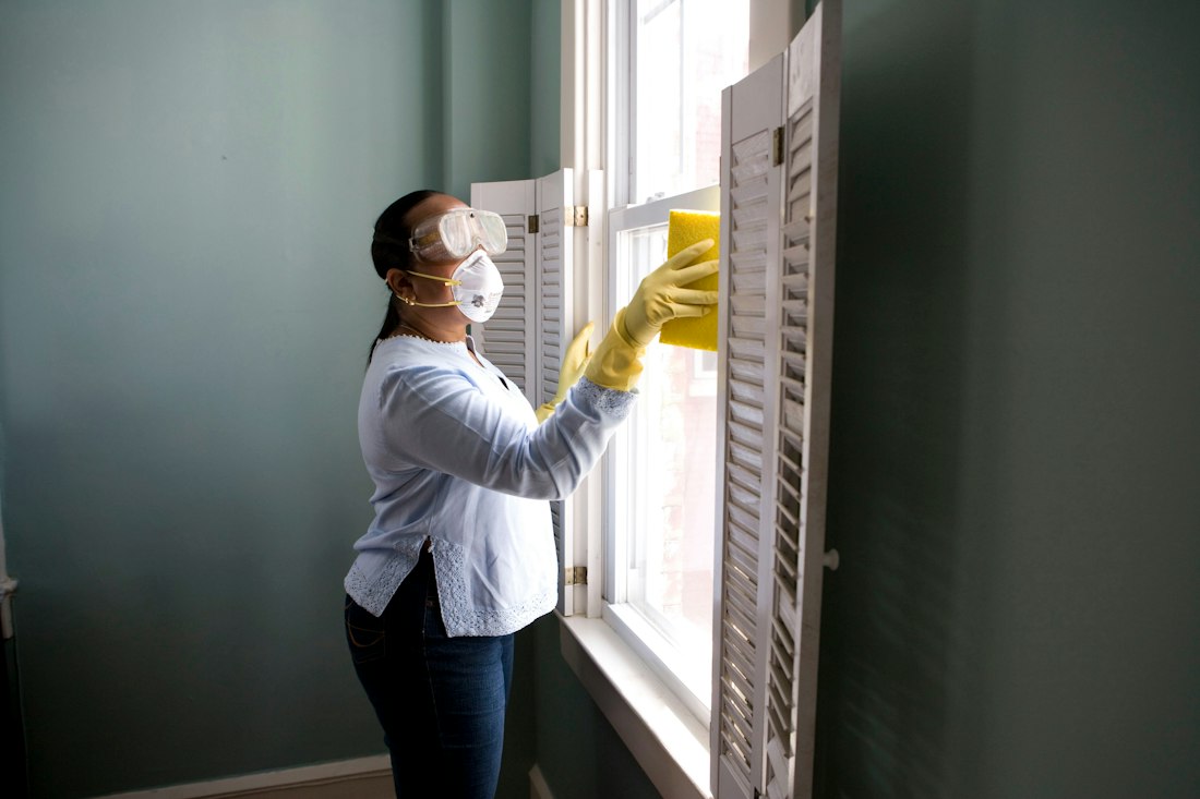 A cleaner wiping a tall window in a bright living room
